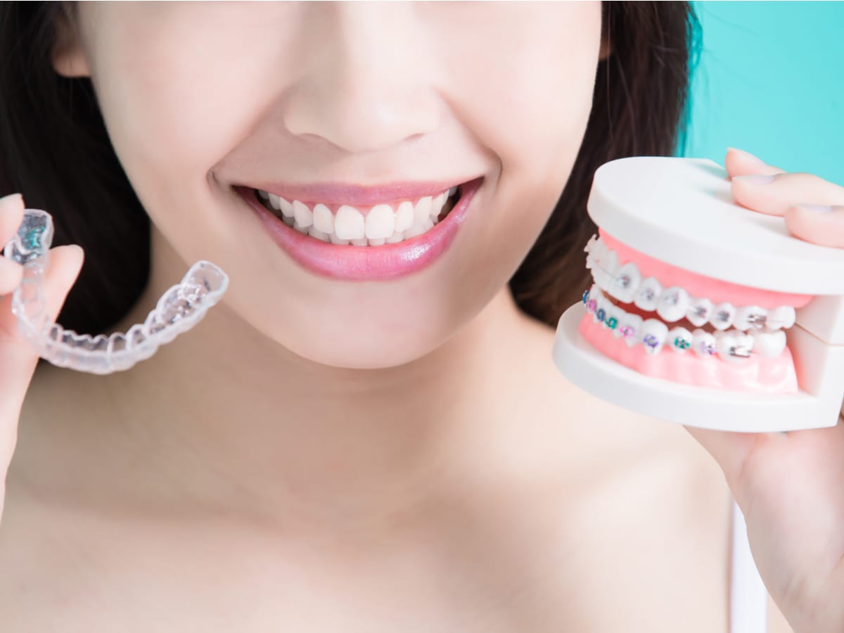 A smiling woman holding braces and invisalign